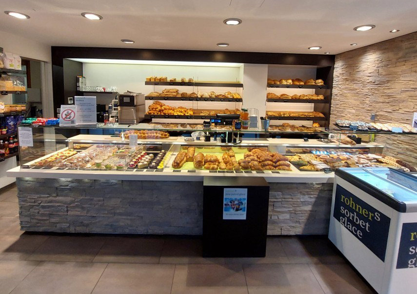 Eine moderne Bäckerei mit einer Auslage voller verschiedener Brote, Gebäck und Desserts, sowie einem Bereich für Sorbets und Getränken.